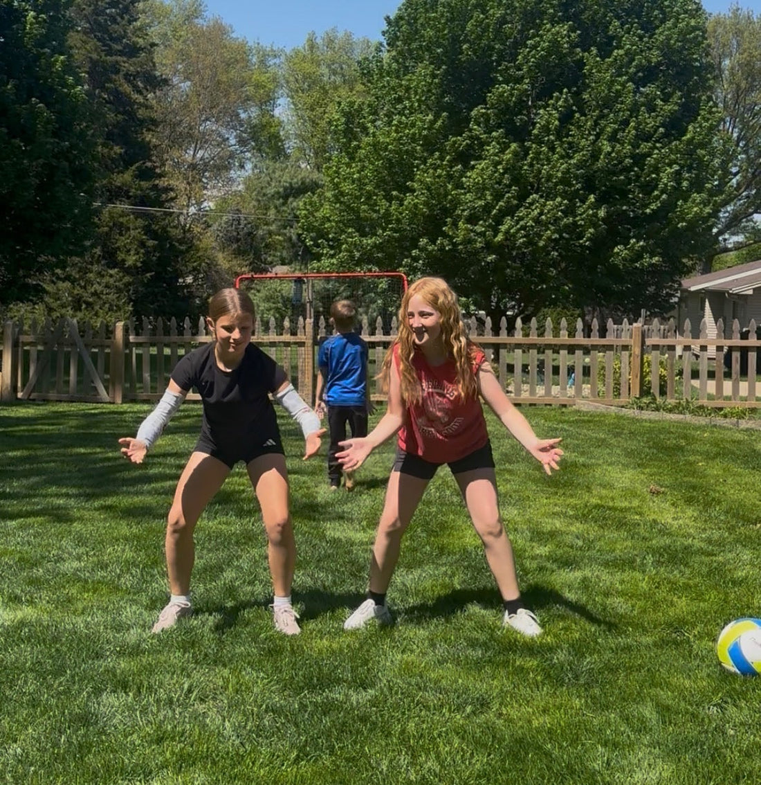 Three young volleyball players in ready position on a sunny backyard lawn