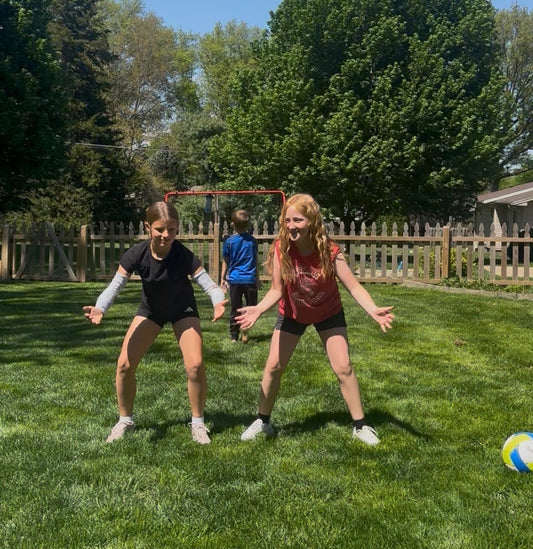 Three young volleyball players in ready position on a sunny backyard lawn